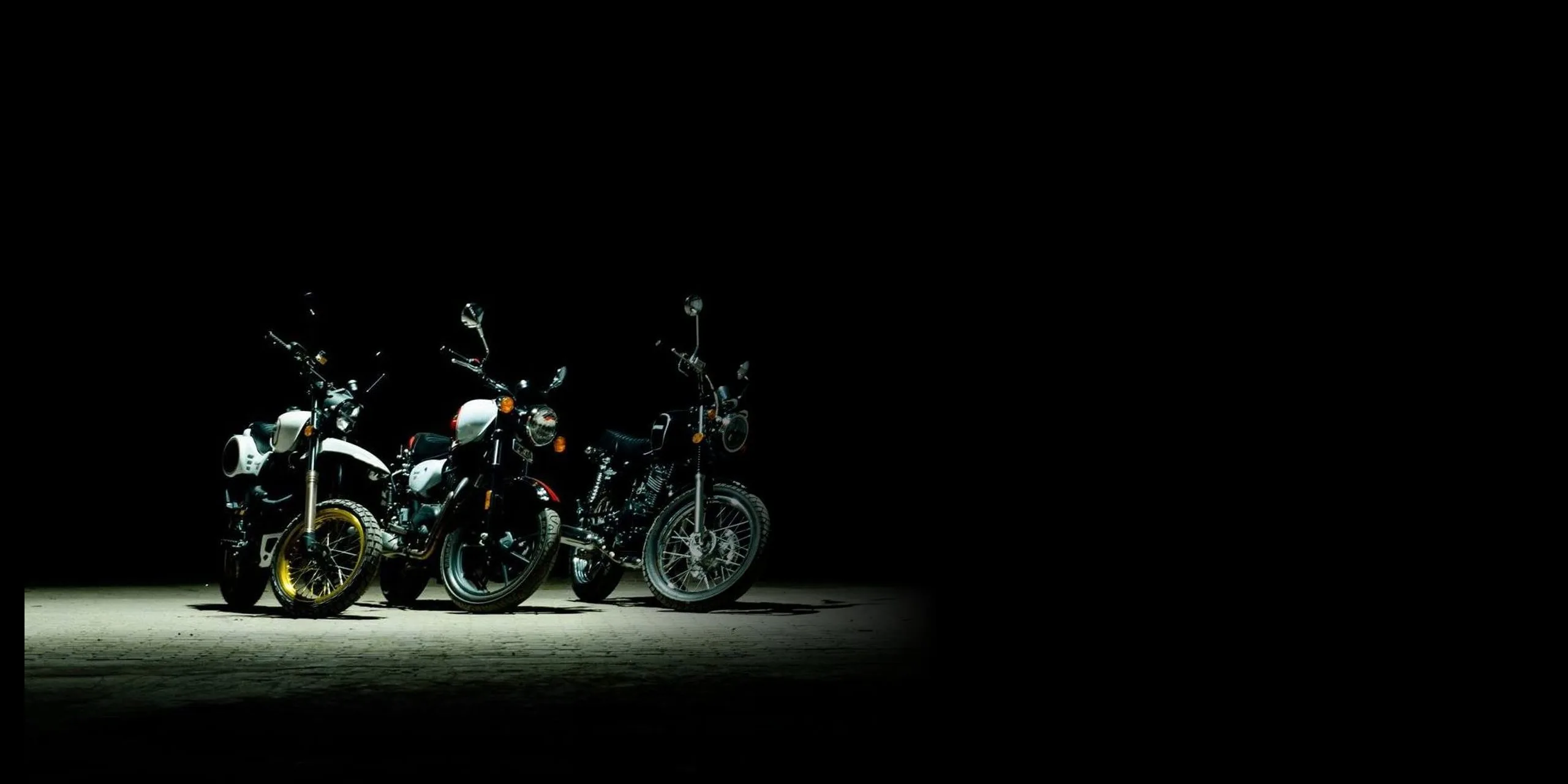 Three Sothassi motorcycles under a single light in the dark